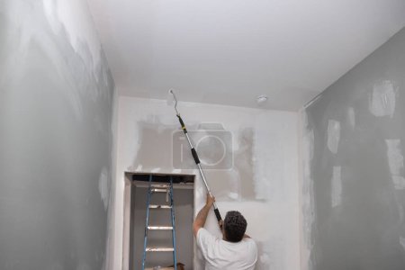 Téléchargez les photos : Mettre à jour améliorer la pièce d'appartement pendant qu'il est en cours de réparation des murs de peinture principale avec peinture à rouleau blanc - en image libre de droit