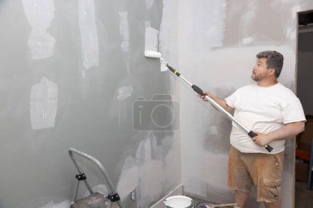 Photo for Update improvement for an apartment room during repair process, master painting walls with roller white paint - Royalty Free Image