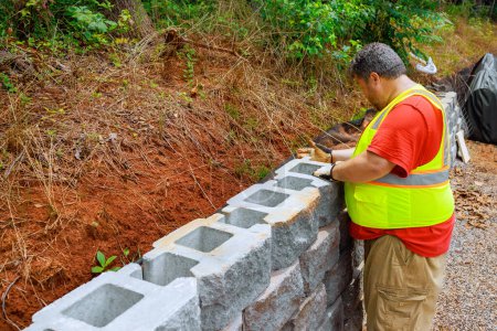 Téléchargez les photos : Travailleur de la construction montait des blocs de béton au mur de soutènement sur le chantier - en image libre de droit