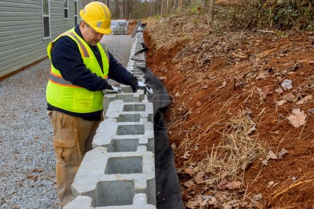 Construction worker is mounting retaining wall using concrete blocks to ensure its proper placement.