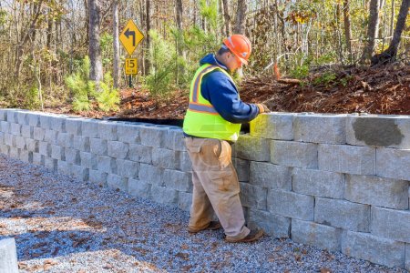 During development of new property, construction worker is using cement blocks for building retaining wall.