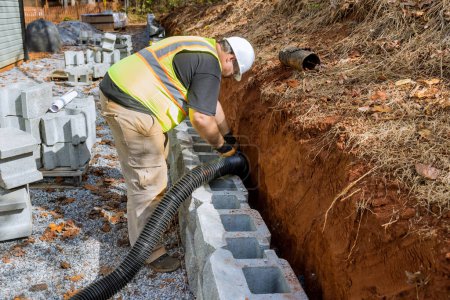 Téléchargez les photos : Ingénieur de construction posent tuyau de drainage pour l'eau de pluie dans le mur de soutènement. - en image libre de droit