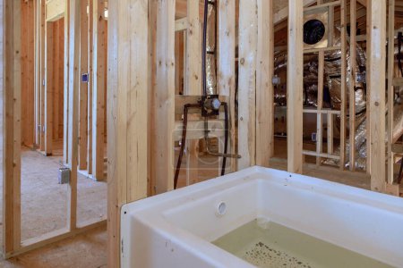 Téléchargez les photos : Maison en construction avec nouvelle baignoire en acrylique entre poutres cadre dans une salle de bain - en image libre de droit