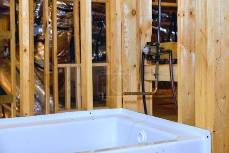 Téléchargez les photos : Maison en construction avec nouvelle baignoire en acrylique installée entre les poutres cadre dans la nouvelle salle de bain - en image libre de droit