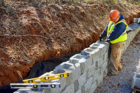 Téléchargez les photos : Travailleur de la construction utilise des blocs de ciment pour la construction mur de soutènement pendant le développement de nouvelles propriétés. - en image libre de droit