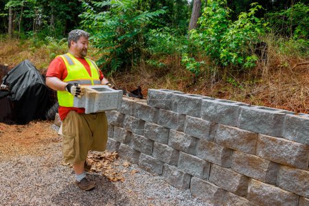 Téléchargez les photos : Travaillant avec diligence, le travailleur de la construction a soulevé le bloc de ciment pour retenir le mur de béton - en image libre de droit
