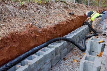 Téléchargez les photos : Entrepreneur travailleur de pose de tuyaux de drainage pour l'eau de pluie dans le mur de soutènement. - en image libre de droit