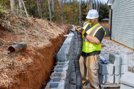 Téléchargez les photos : Travailleur de la construction de pose de tuyaux de drainage pour l'eau de pluie pendant le montage mur de soutènement. - en image libre de droit