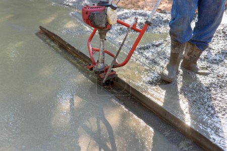 Photo for Tamping machine is used to align fresh concrete compacted layer in new driveway that is being constructed - Royalty Free Image