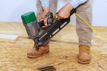 Téléchargez les photos : Utilisation d'un pistolet à ongles d'air pour installer du contreplaqué de bois sur le sol de la nouvelle maison - en image libre de droit