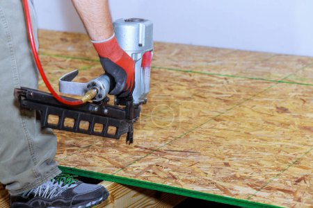 Téléchargez les photos : Nouvelle maison avec installation de contreplaqué en bois au sol à l'aide d'un pistolet à ongles - en image libre de droit