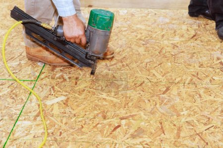 Téléchargez les photos : Installation de contreplaqué en bois pour l'utilisation au sol d'un pistolet à clous pneumatique dans une nouvelle maison - en image libre de droit