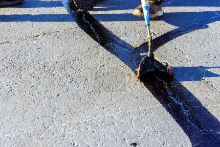 Durante el patcher trabajador realiza relleno recubierto grietas de asfalto sellado betún emulsión carretera trabajo de restauración de la superficie