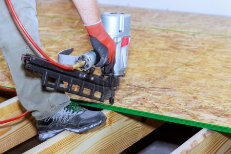 Téléchargez les photos : Dans l'installation de plancher de contreplaqué en bois nouvelle maison à l'aide de pistolet à ongles - en image libre de droit