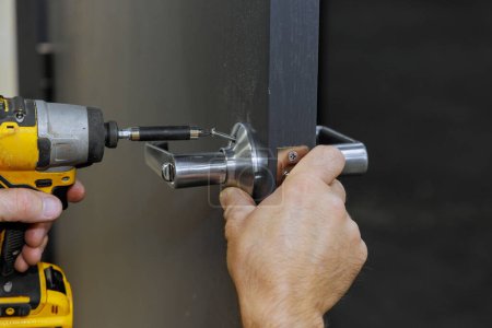 Téléchargez les photos : À l'aide d'un tournevis, charpentier installe des poignées de verrouillage sur la porte de la pièce - en image libre de droit