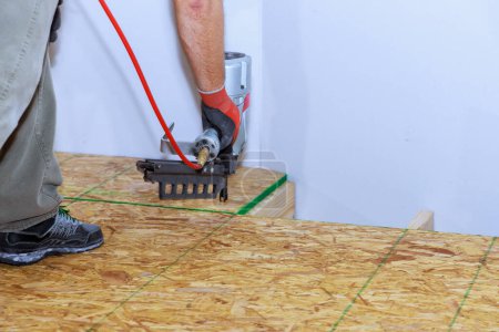 Téléchargez les photos : Installation de plancher de contreplaqué en bois dans une nouvelle maison à l'aide d'un pistolet à ongles - en image libre de droit