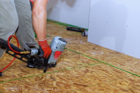 Téléchargez les photos : Utilisation d'un pistolet à ongles pneumatique pour installer du contreplaqué de bois pour les revêtements de sol dans une nouvelle maison - en image libre de droit