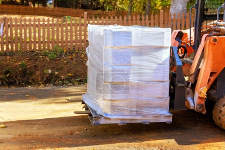 Photo for Worker with small forklift unloads pallet concrete blocks for retaining walls - Royalty Free Image