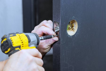 Téléchargez les photos : Installation de poignées de verrouillage avec tournevis sur la porte de la pièce par charpentier - en image libre de droit