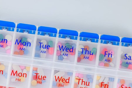 Una caja organizadora semanal para la dispensación de medicamentos sobre fondo blanco se muestra con cápsulas de medicamentos dentro.