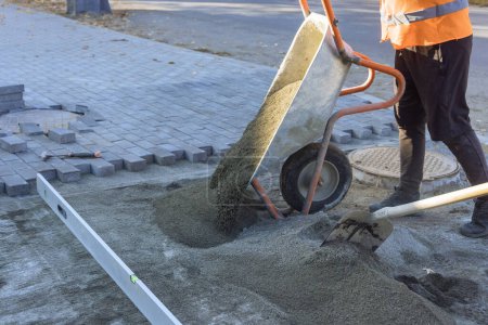 Téléchargez les photos : Utilisation brouette pour jeter du sable sur le sentier en préparation pour la pose de pierres décoratives - en image libre de droit