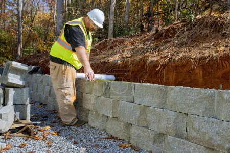 Travailleur a étudié les plans directeurs lors du montage des murs de soutènement à l'aide de blocs de ciment