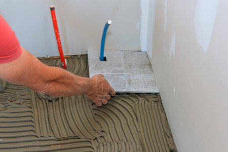On bathroom floor tiler is placing ceramic tiles over adhesive