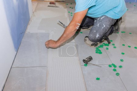 Tiler is laying large ceramic floor tile over mortar adhesive glue