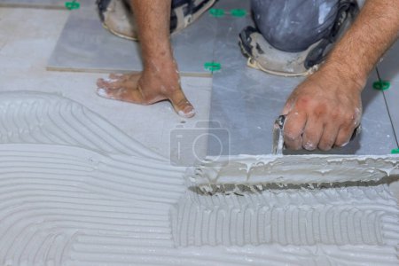 Tiler applies adhesive mortar cement plaster to floor in preparation for installation of ceramic tiles