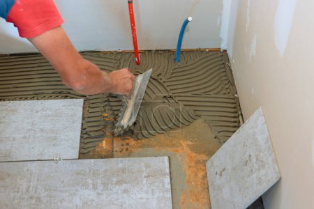 Photo for Preparing concrete floor for tiling by troweling adhesive onto surface - Royalty Free Image