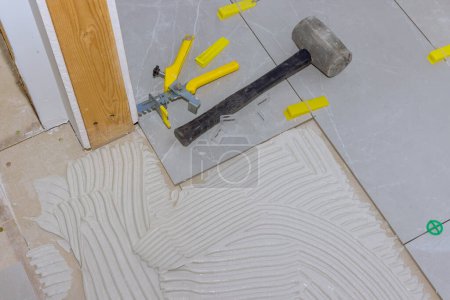 Durante la instalación de grandes baldosas, tiler trabaja sobre adhesivo de mortero que une baldosas de cerámica de piso juntos