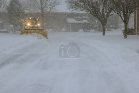 An ice plough removes snow from parking lot during heavy snowfall snowstorm
