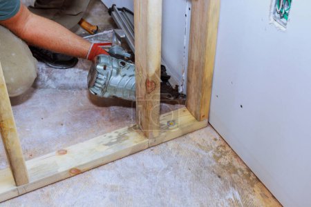 Builder is using an air hammer to nail wooden beams to housing frame