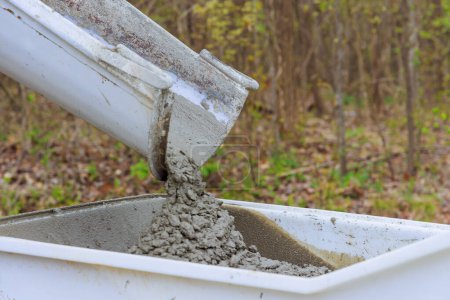 Baustelle mit nassem Zement, der von einer Zement-LKW-Rutsche in einen Schubkarrenbahnbeton-Buggy fällt