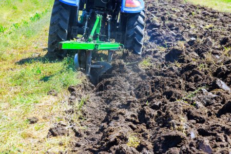 An agricultural tractor plowing field is cultivating soil at preparation for planting of grain in spring
