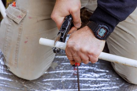 Technician plumber cuts a plastic PVC pipe by special scissors