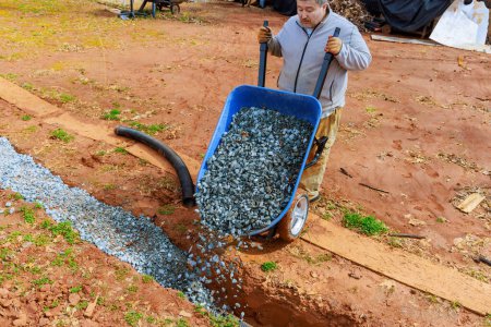 Crushed stone is fills into drainage pipe from wheelbarrow by worker