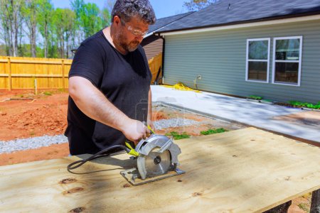 Carpenter trimming plywood board with handsaw