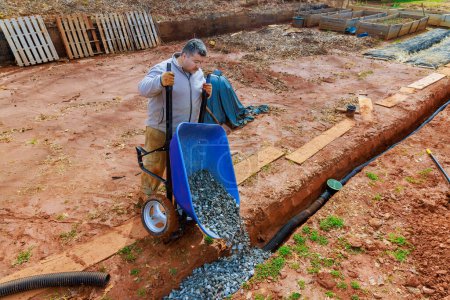 Worker fills drainage pipe with crushed stone from wheelbarrow