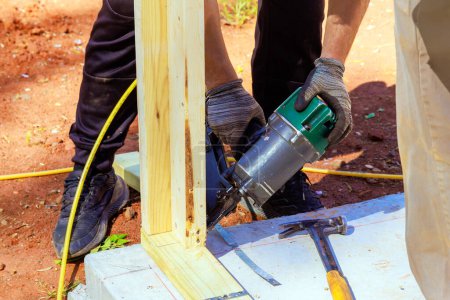 Framer uses an air nail hammer to install beams in wooden frame
