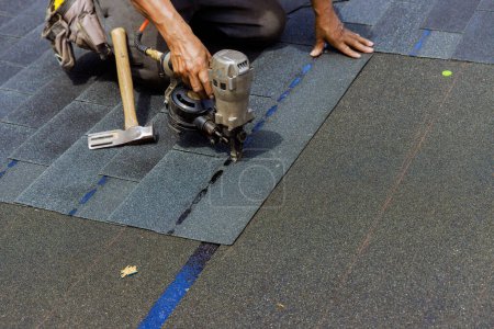 An air nail gun is used by construction worker to install new bitumen shingles on roof