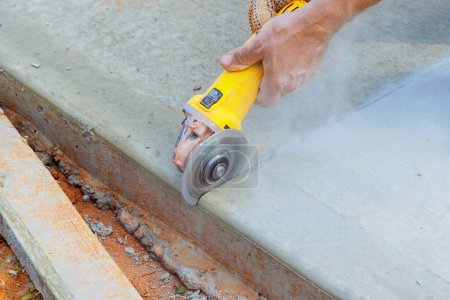 An employee of construction industry cuts concrete foundation after it has been poured using cutting machine grinder