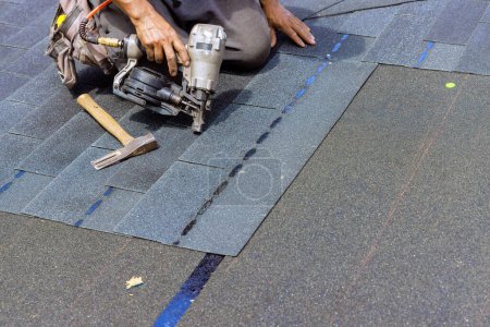 Photo for Installing new bitumen shingles using an air nail gun on roof of house - Royalty Free Image