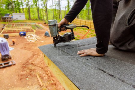 Instalación de nuevas tejas de betún de asfalto en el techo con pistola neumática de clavos de aire