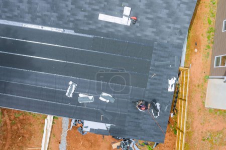 Photo for Roofer installing new asphalt bitumen shingles with air nail guns - Royalty Free Image