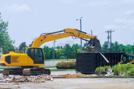 On construction site, an excavator loads construction concrete waste into disposal container