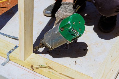 Photo for Framer worker installing beams using air nails hammer in nailing wooden frame - Royalty Free Image