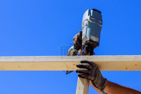 Framer uses an air nail hammer to install beams in wooden frame