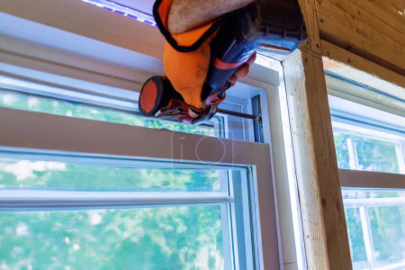 In new house, construction worker installs plastic windows using screwdriver