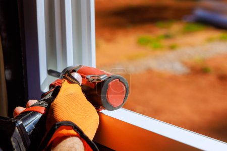 Construction worker is installing plastic windows with screwdriver in newly constructed home